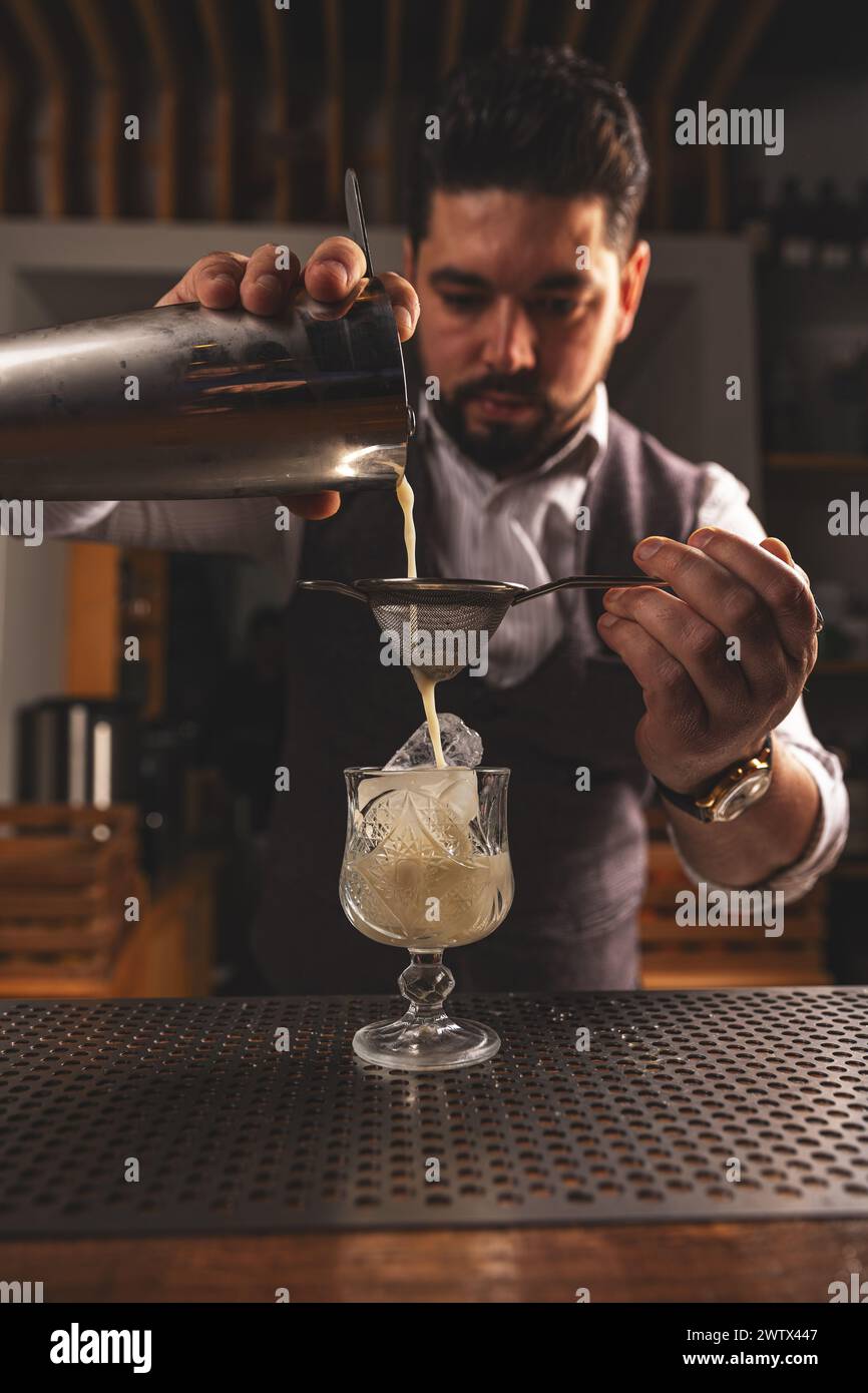 Focused bartender pours a mixed drink through a strainer into a glass