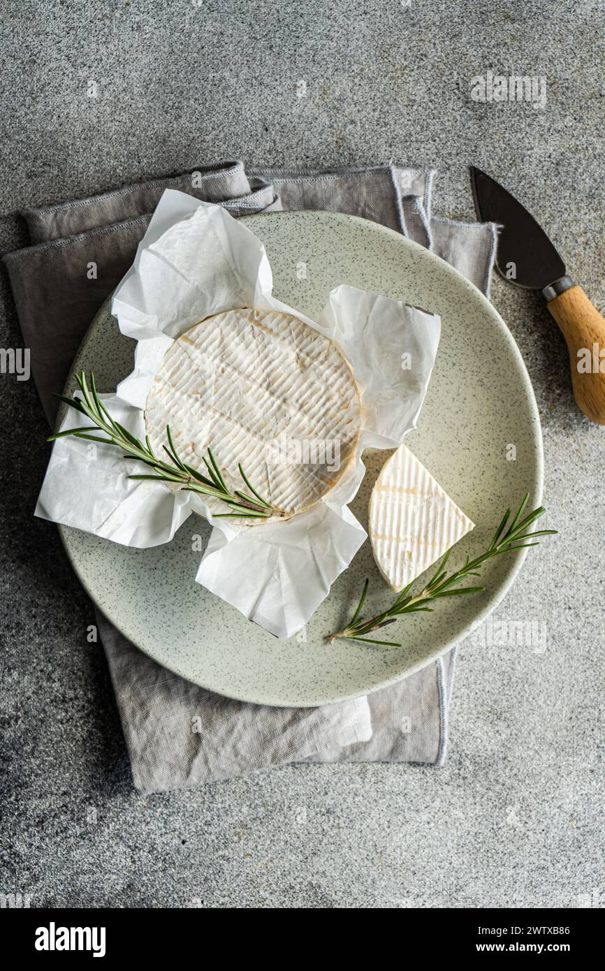Overhead view of a whole brie with fresh rosemary on a plate and folded napkin Stock Photo