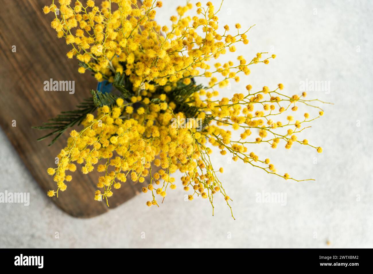 Overhead view of a bunch of yellow mimosa stems in a vase on a wooden chopping board Stock Photo