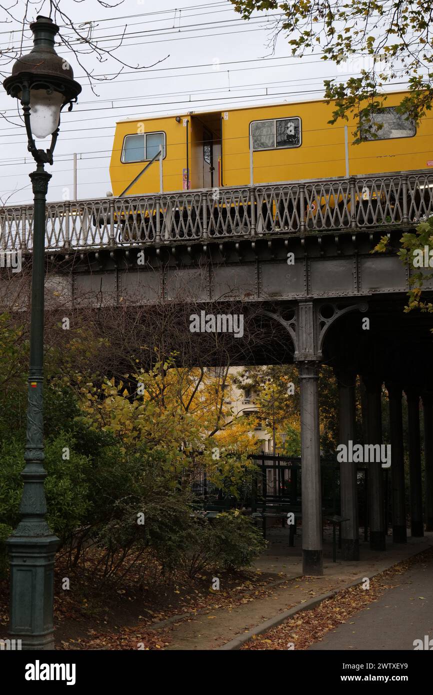 Yellow train crossing a bridge. Yellow train crossing the park next to a streetlight Stock Photo