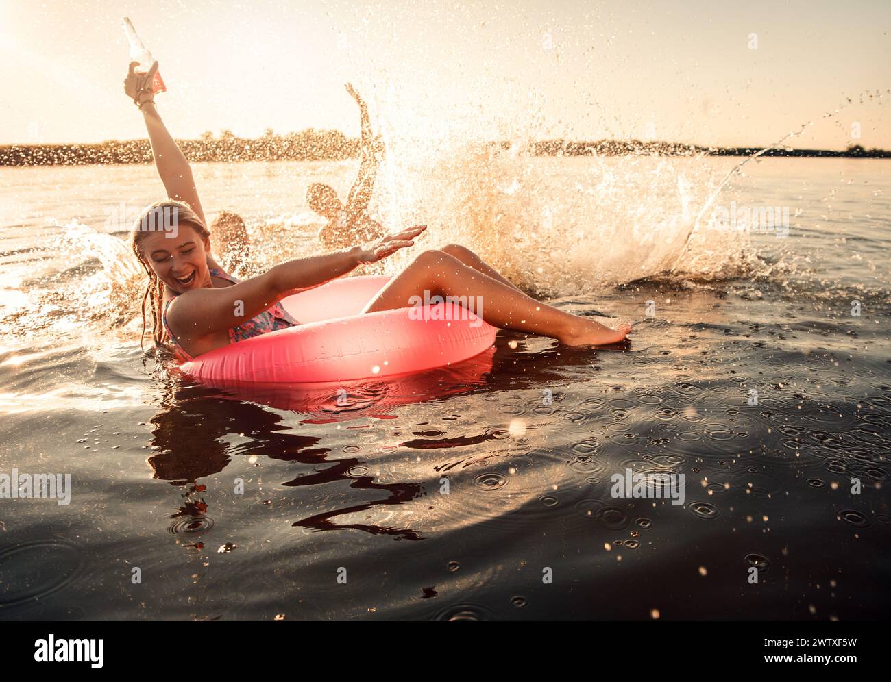 Friends having fun enjoying a summer day swimming and jumping at the lake. Stock Photo