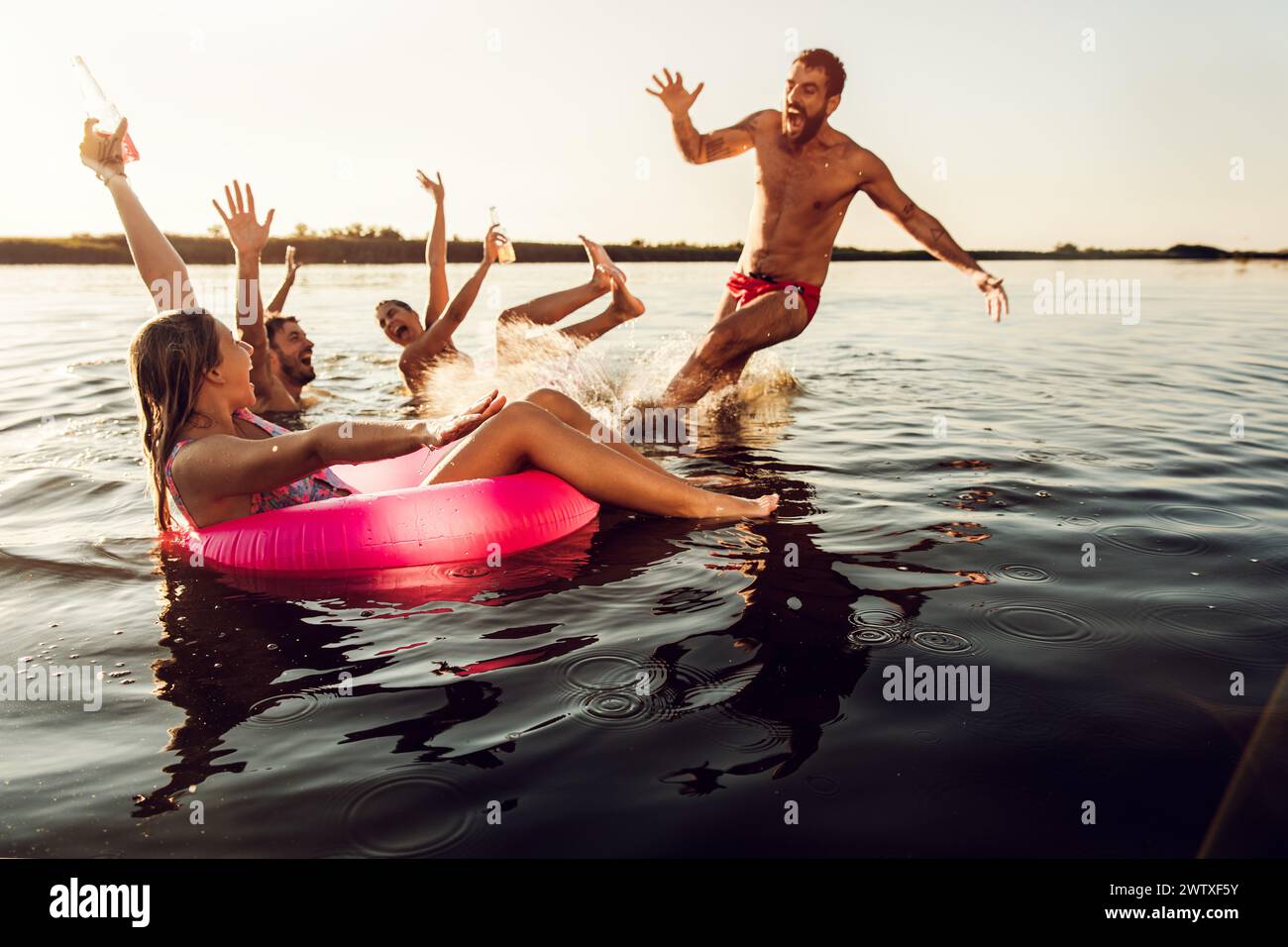 Friends having fun enjoying a summer day swimming and jumping at the lake. Stock Photo