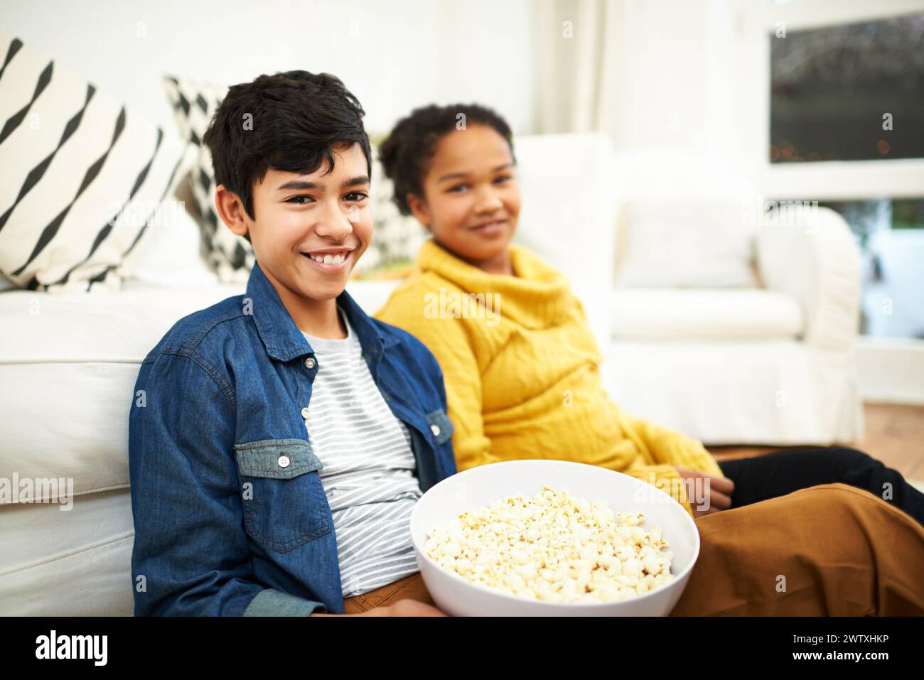Happy family, love and popcorn in portrait in home and relax for bonding together on vacation. Brother, sister and positive face of siblings by couch Stock Photo