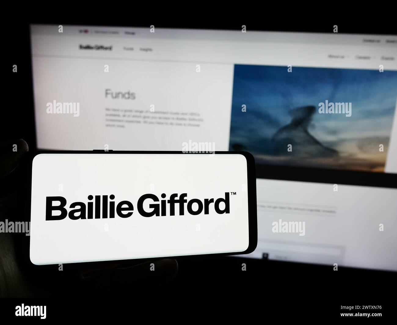 Person holding mobile phone with logo of British investment management