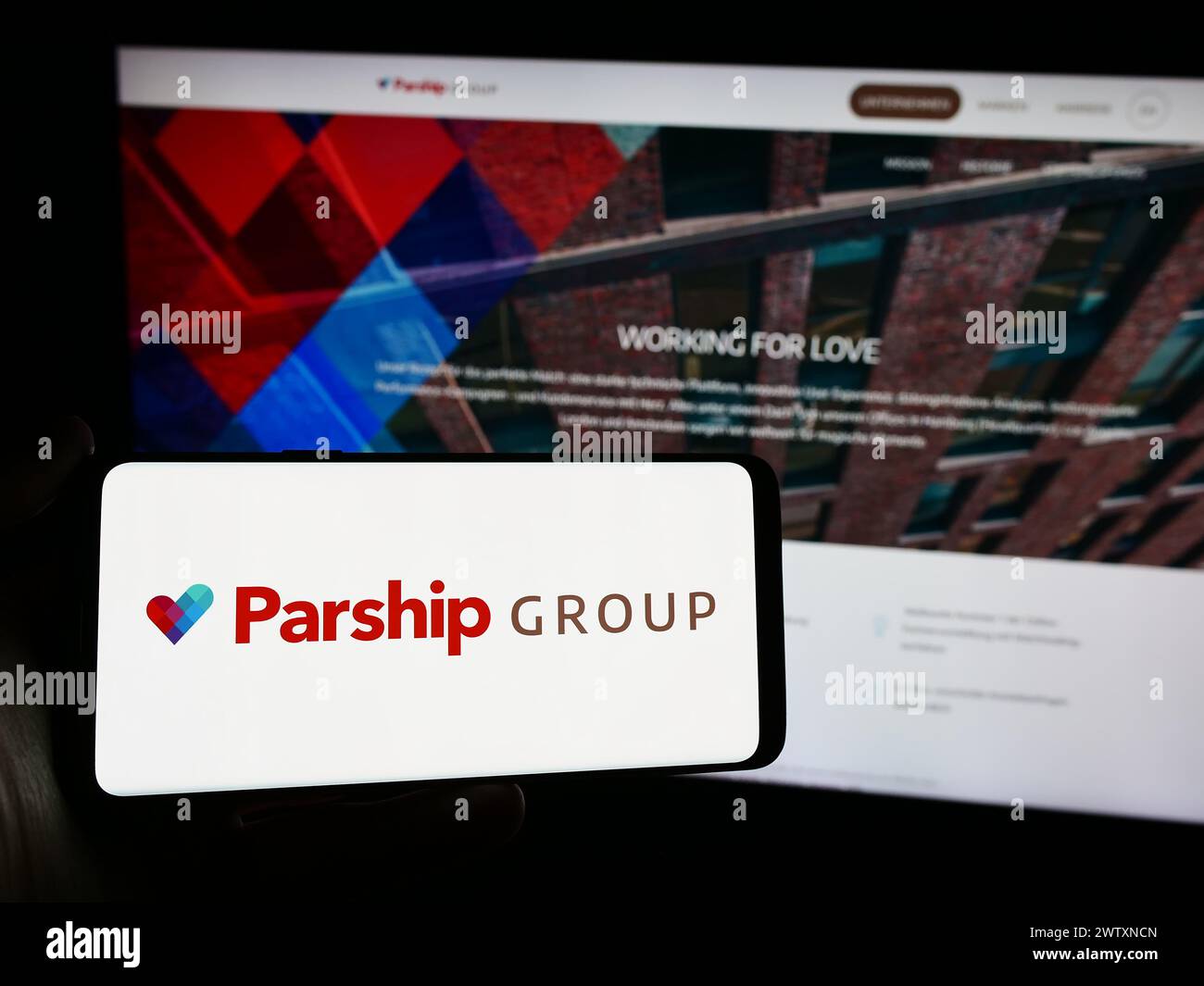 Person holding smartphone with logo of German online dating company ParshipMeet Holding GmbH in front of website. Focus on phone display. Stock Photo