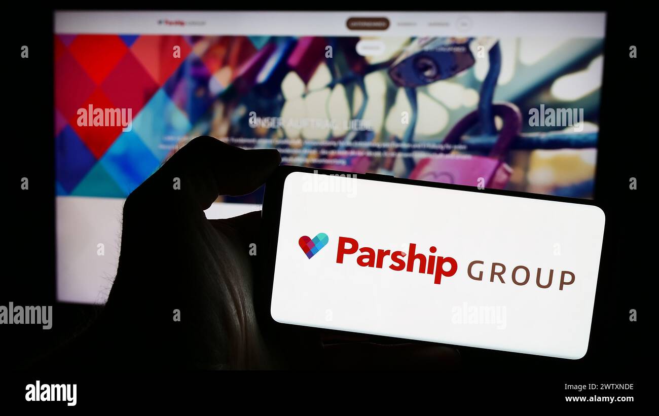 Person holding mobile phone with logo of German online dating company ParshipMeet Holding GmbH in front of web page. Focus on phone display. Stock Photo