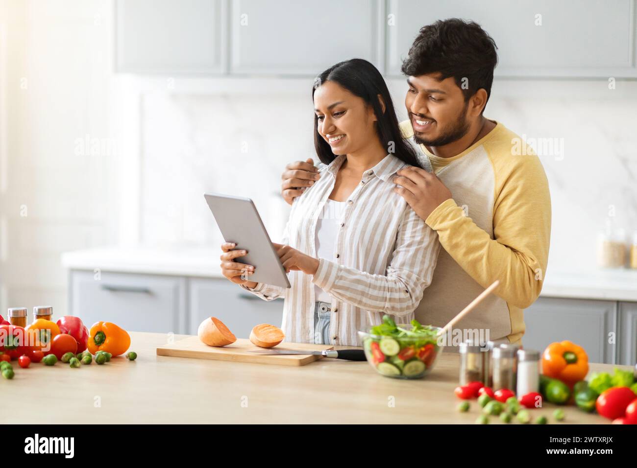 Happy loving young indian spouses using digital tablet while cooking Stock Photo