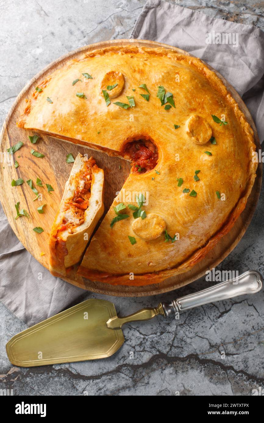 Empanada gallega is a traditional savory pie from the Spanish filling is with meat, bell pepper, tomato and onion closeup on the board on the table. V Stock Photo