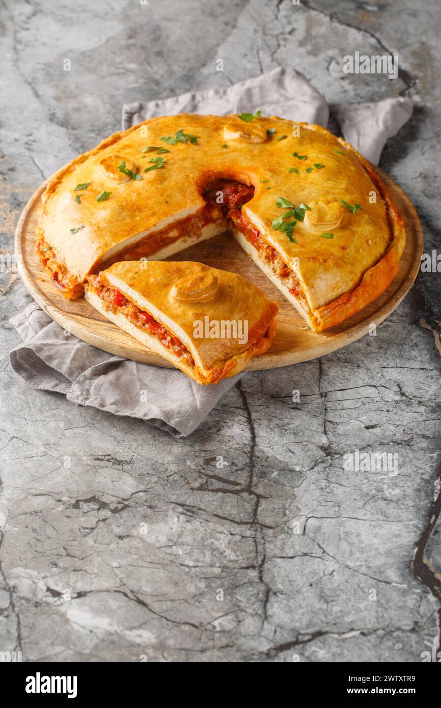 Empanada gallega is a traditional savory pie from the Spanish filling is with meat, bell pepper, tomato and onion closeup on the board on the table. V Stock Photo