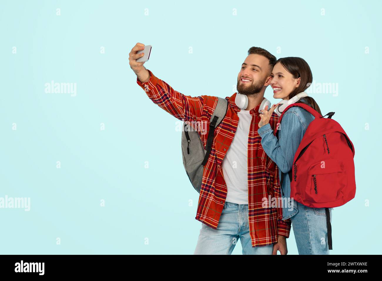 Cheerful college couple with smartphone snapping selfies against blue backdrop Stock Photo