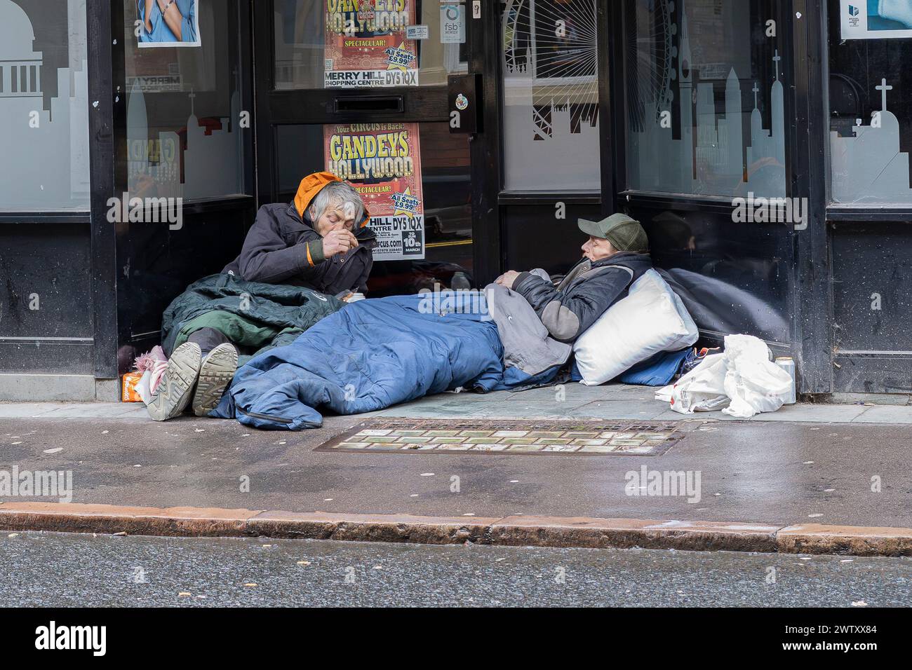 Stourbridge, UK. 20th March, 2024. UK weather: trying to stay warm and dry on a damp and overcast day in Stourbridge, West Midlands. Two gentlemen seek refuge in a vacant shop doorway to shelter from the rain. Credit: Lee Hudson/Alamy Live News Stock Photo