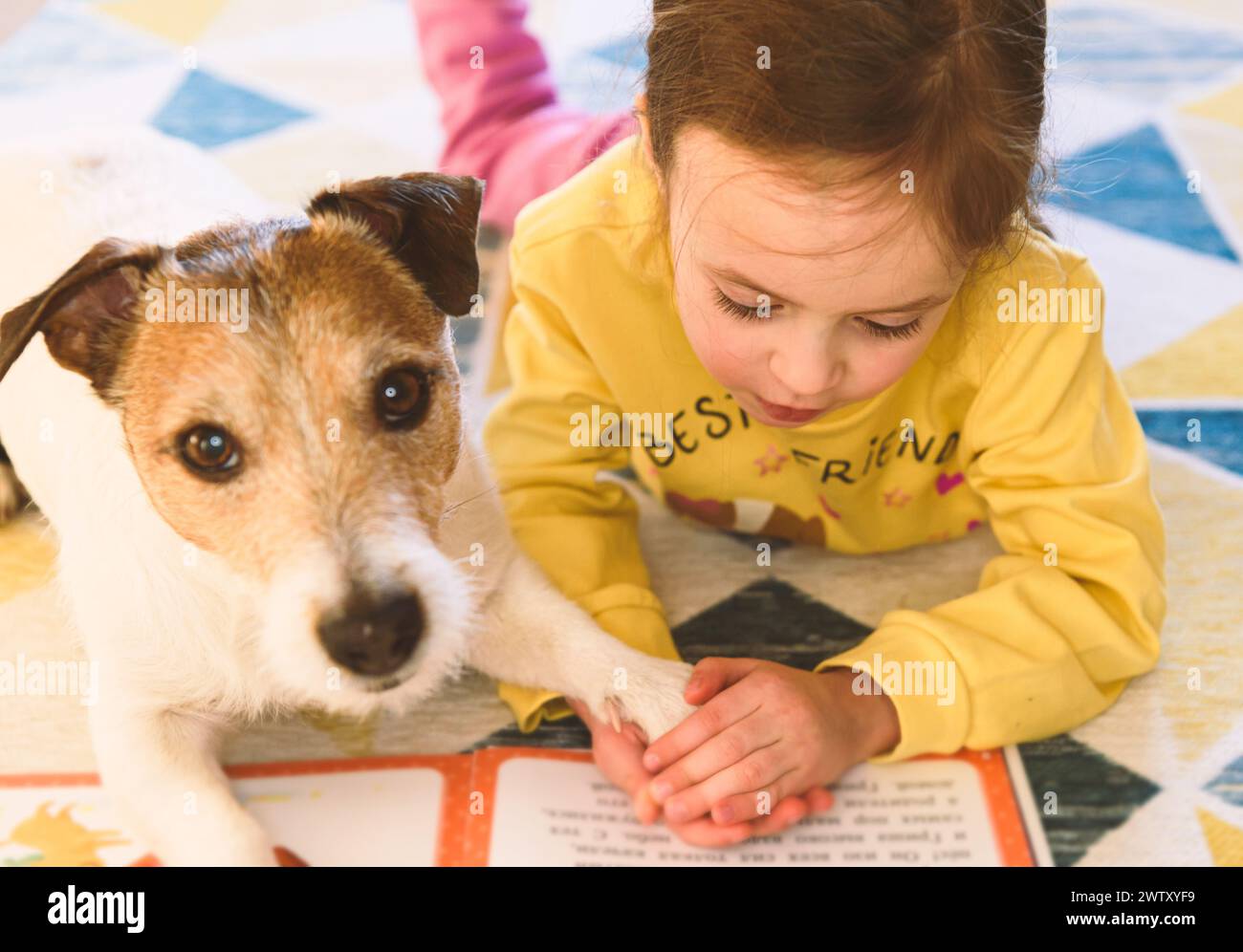 Small girl learning to read. Kid is reading a book to her pet dog. Stock Photo