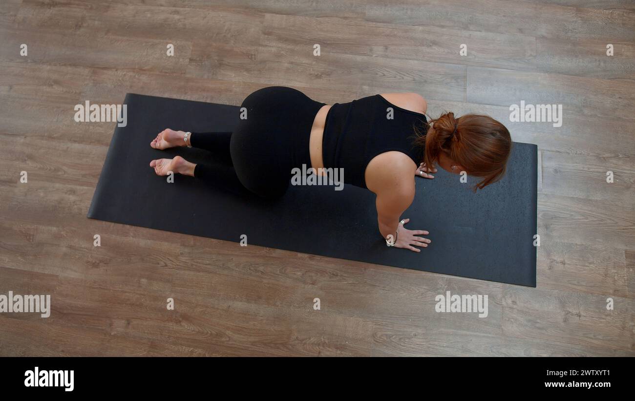 Beautiful sporty girl practicing yoga or pilates at home. Media. Top view of a woman doing balance exercise and stretching her arm and leg. Stock Photo