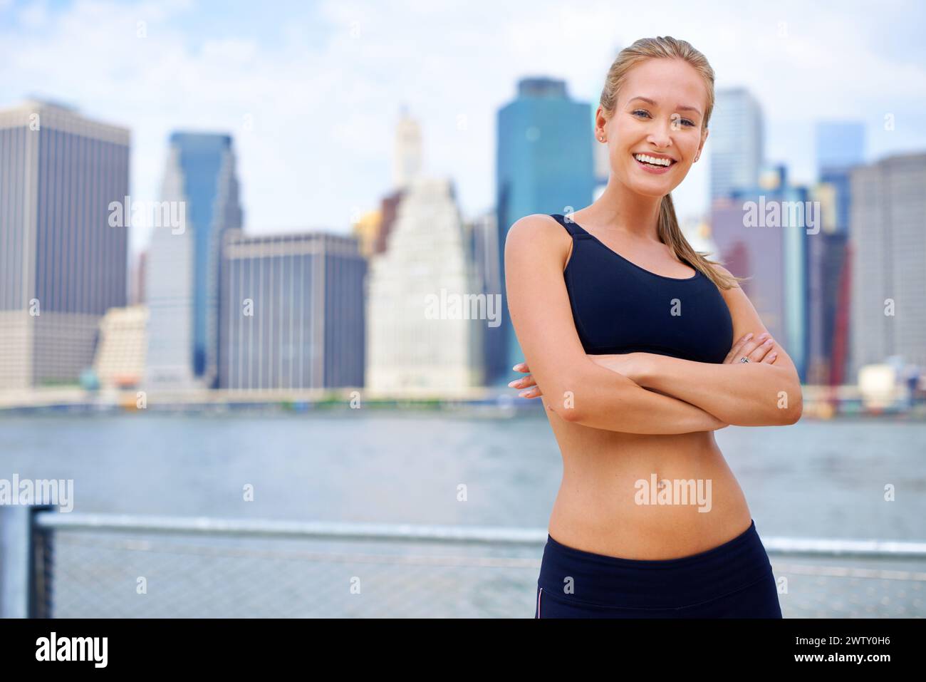 Woman and smile at river side with city view on sport clothes to jog, fitness and healthy mindset in New York. Portrait, arms folded and female person Stock Photo