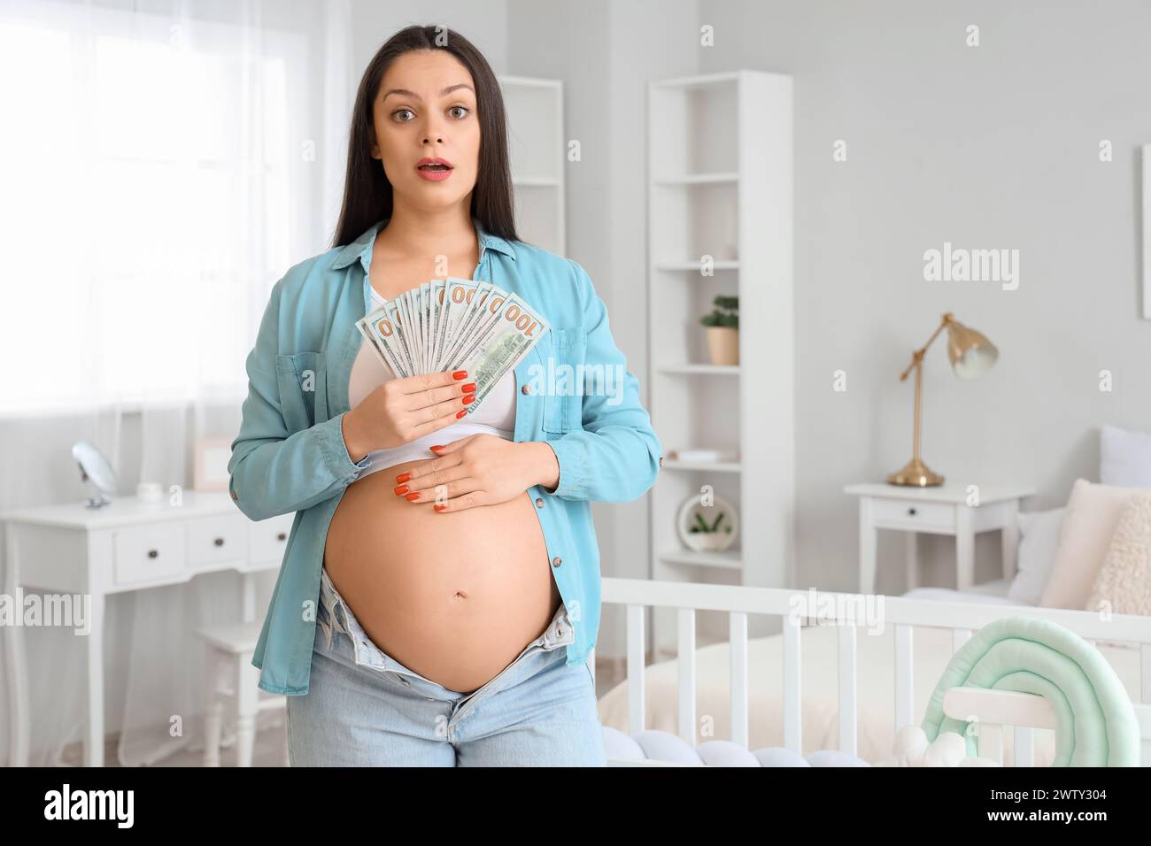 Shocked young pregnant woman with money in children's bedroom. Maternity Benefit concept Stock Photo