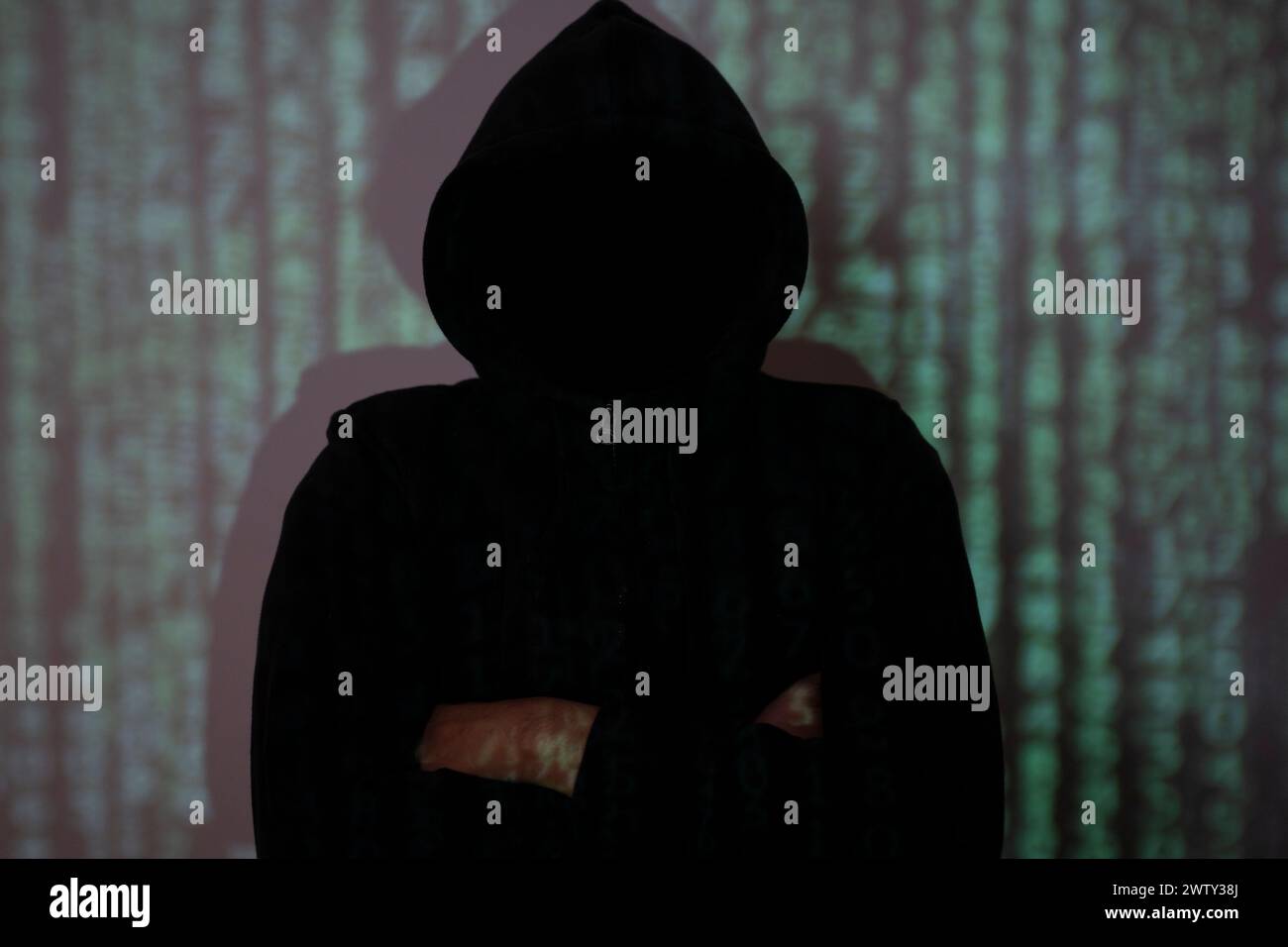 The hacker stood in the shadows with his arms crossed. Stock Photo