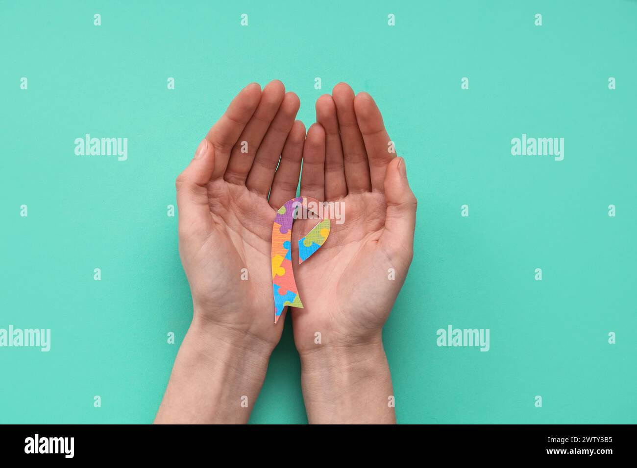 Female hands holding awareness ribbon on cyan background. Autistic ...