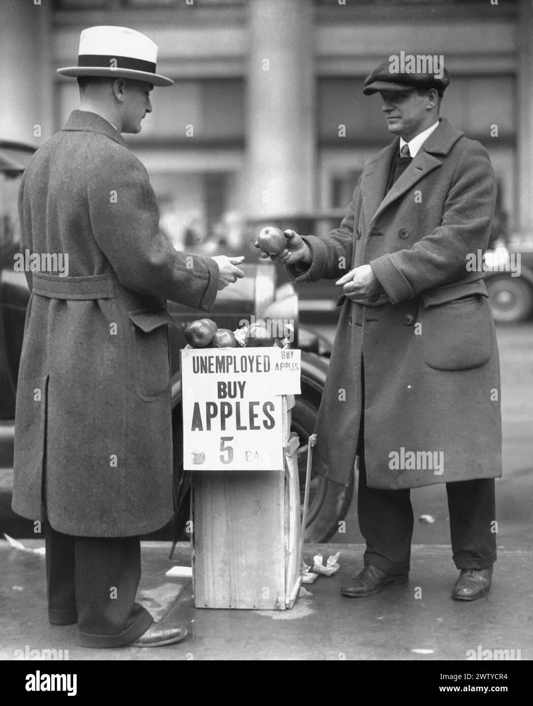 A smartly dressed unemployed man is pictured on the sidewalk selling apples during the depression Stock Photo