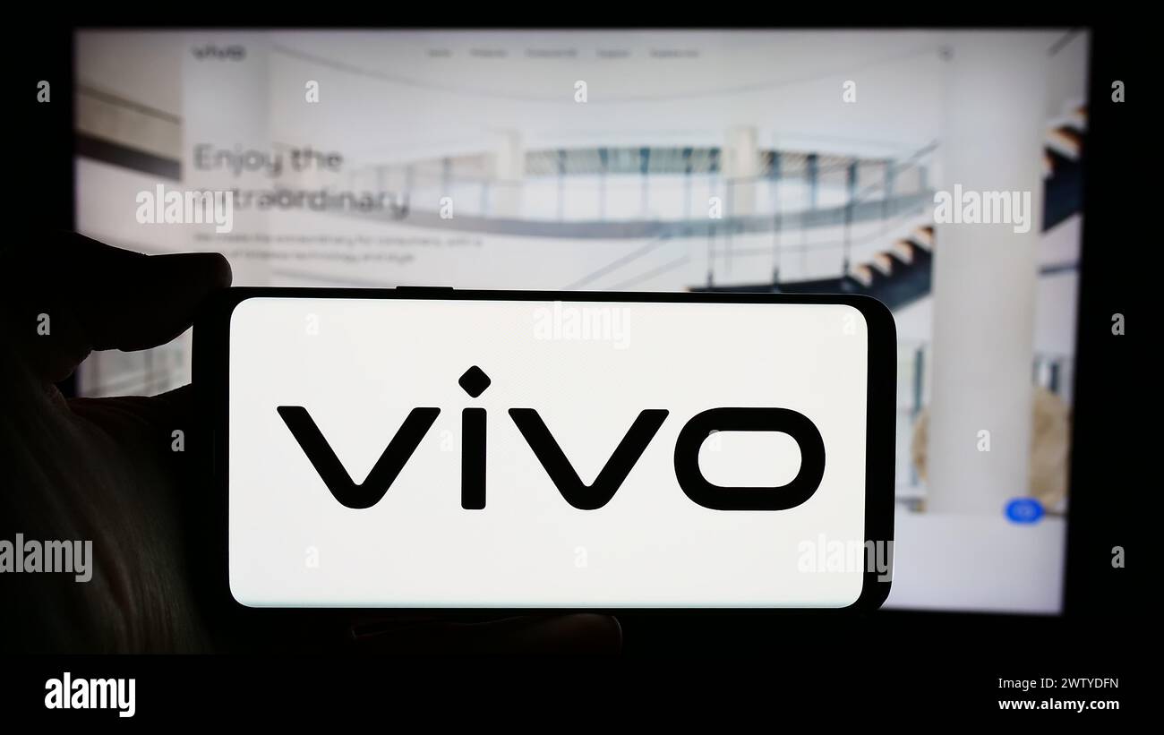 Person holding cellphone with logo of Chinese company Vivo Communication Technology Co. Ltd. in front of webpage. Focus on phone display. Stock Photo