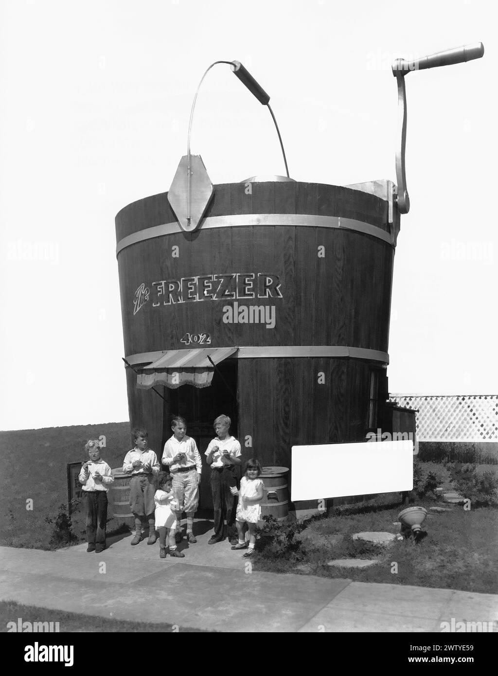 Handful of children standing out front of an ice cream store named The Freezer in the shape of an old fashion bucket with a crank Stock Photo