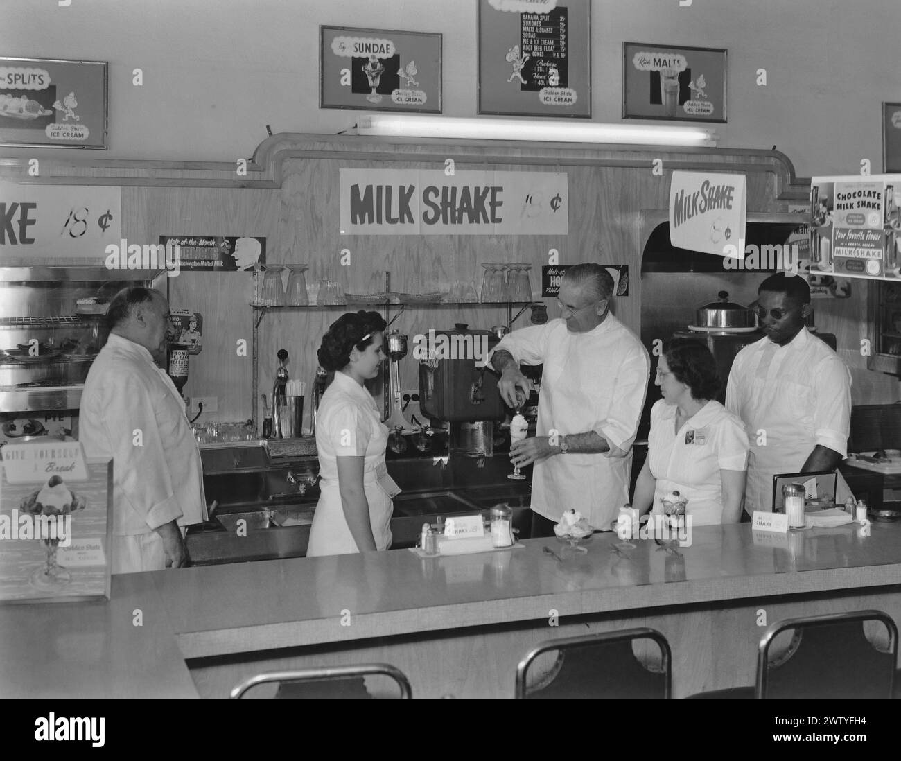 The boss shows employees how to make a milkshake behind the counter of a food cafe Stock Photo
