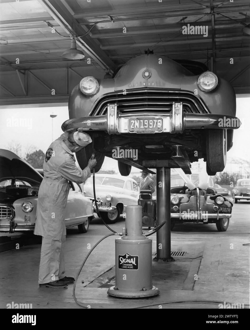 A mechanic greases the joints of an automobile while it's up in the air on a lift at a Signal service station Stock Photo