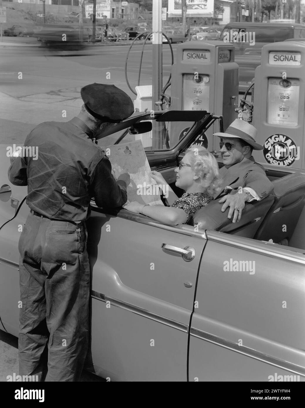A service station attendant helps a couple at the gas pump with directions using a map Stock Photo