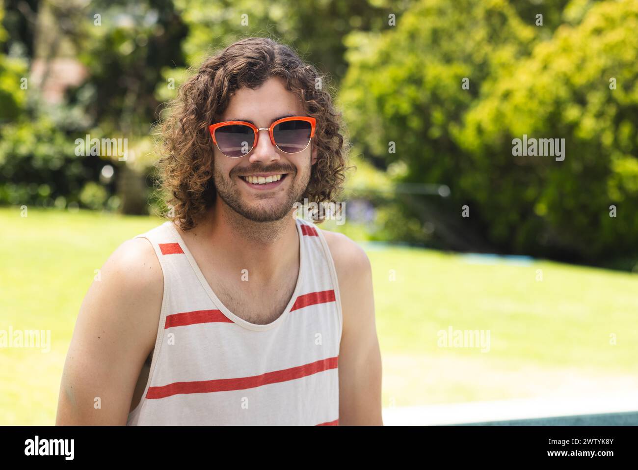 A young Caucasian man with curly hair smiles outdoors with copy space at home Stock Photo