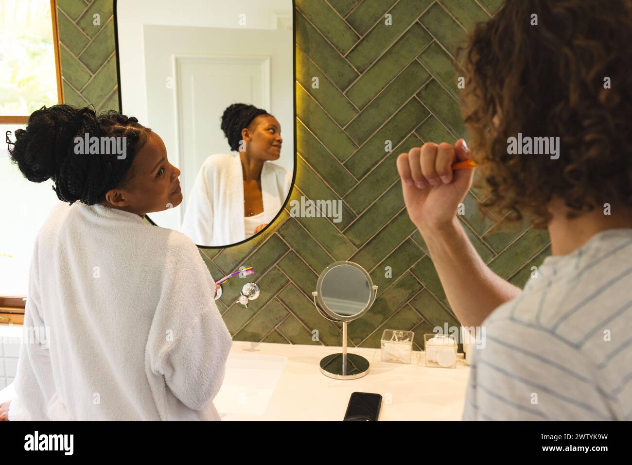 A diverse couple is in well-lit bathroom Stock Photo