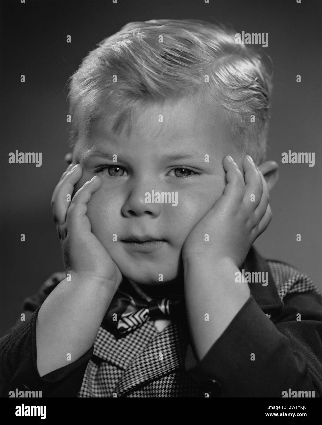 A young boy puts his fingers in his ears to avoid hearing something Stock Photo