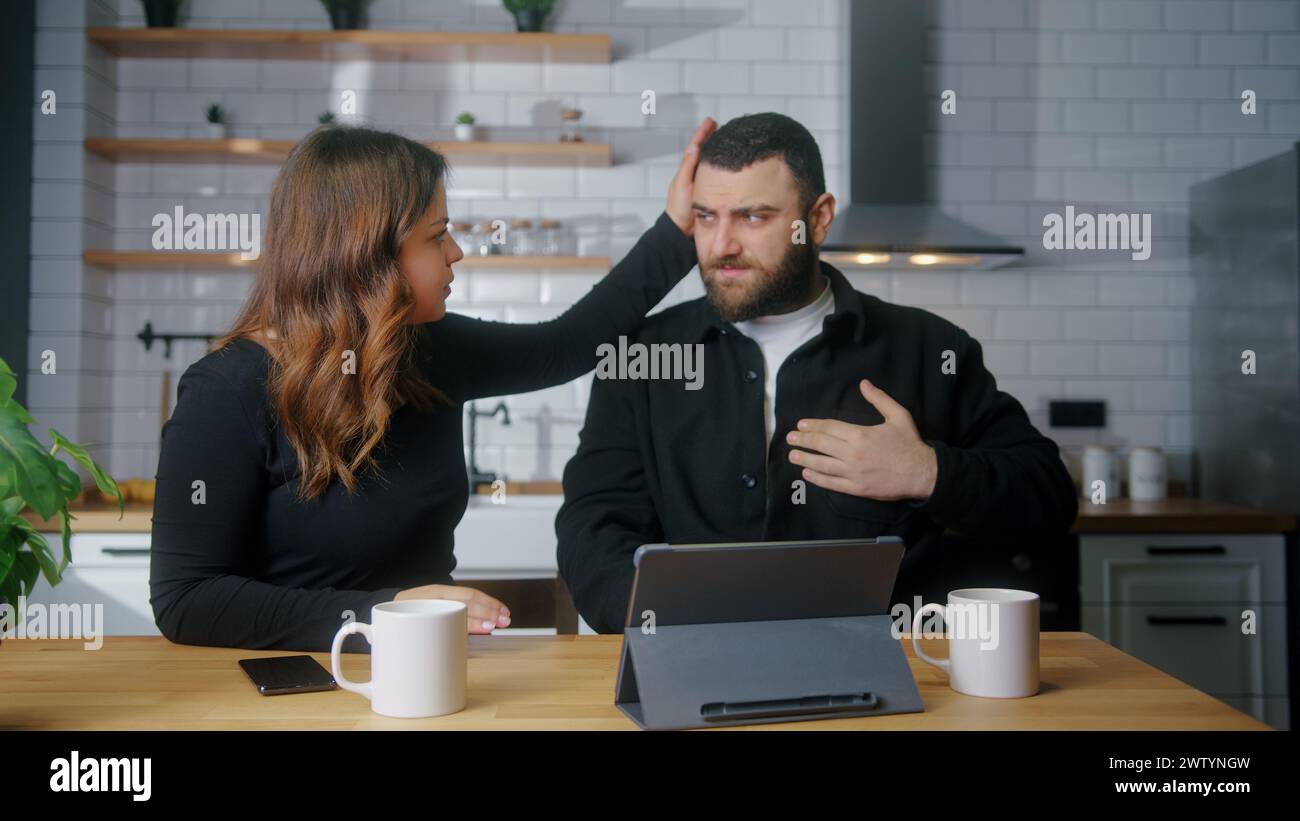 Young couple sit in kitchen while man suffering chest pain, holding massaging his chest, his girlfriend get worry and check him. Health problems conce Stock Photo