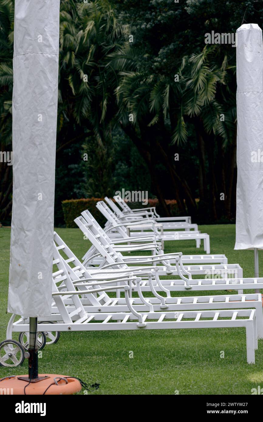 Preparing the hotel area for the summer season, arrangement of outdoor furniture for the relaxation pool area. White plastic sun loungers and umbrella Stock Photo