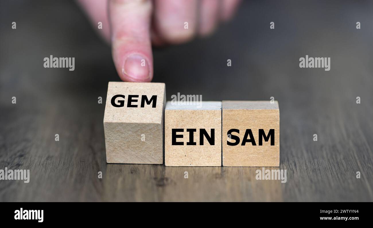 Hand turns wooden cube and changes the German word 'einsam' (lonely) to 'gemeinsam' (together). Stock Photo