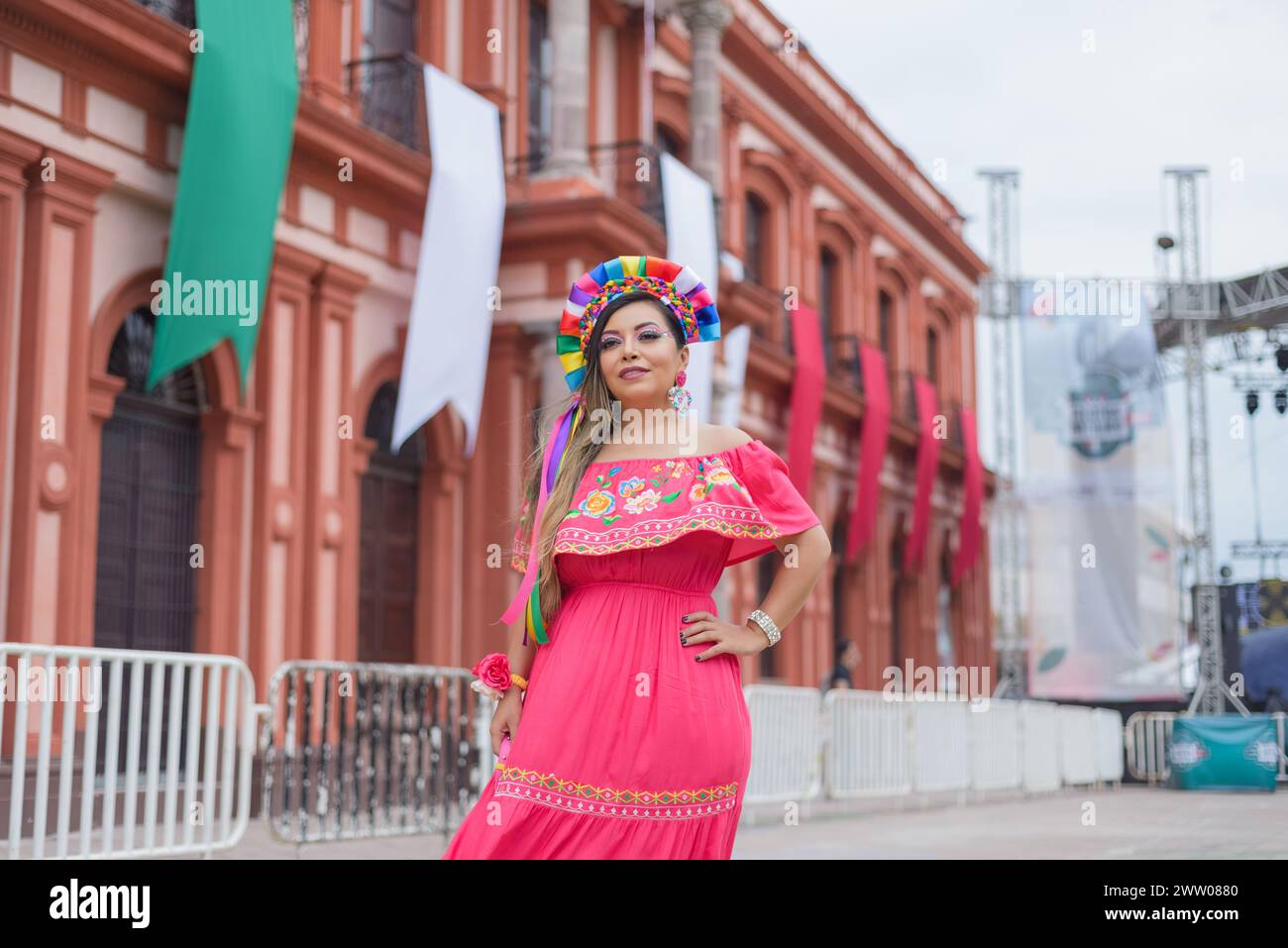 Mexican woman wearing traditional dress. Street decorated with colors of the Mexican flag. Cinco ...