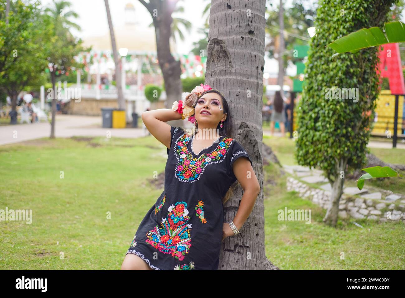 Mexican woman wearing traditional dress. Street decorated with colors of the Mexican flag. Cinco ...