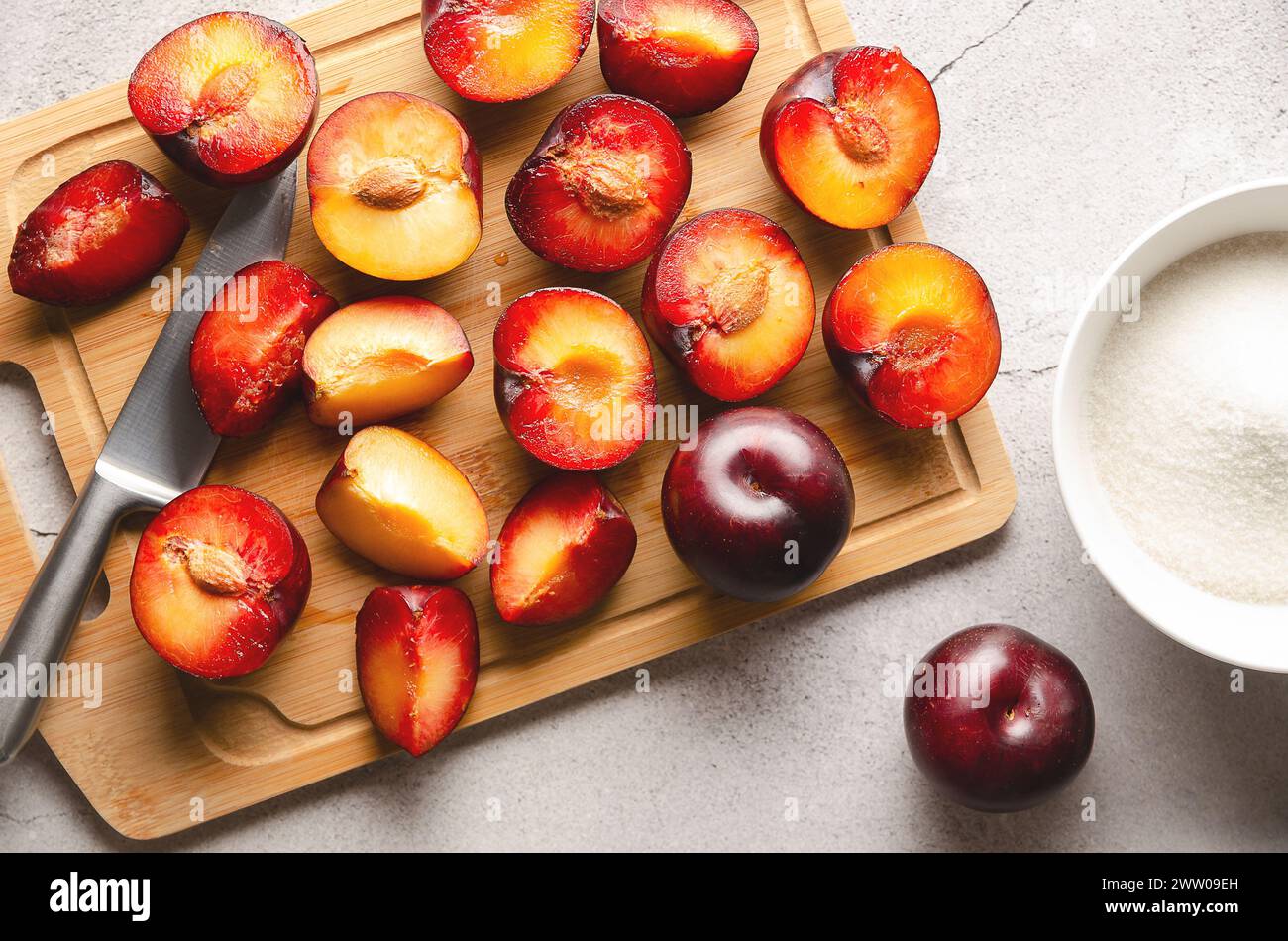 Fresh plums on cutting board with knife and sugar on grey background. Stock Photo