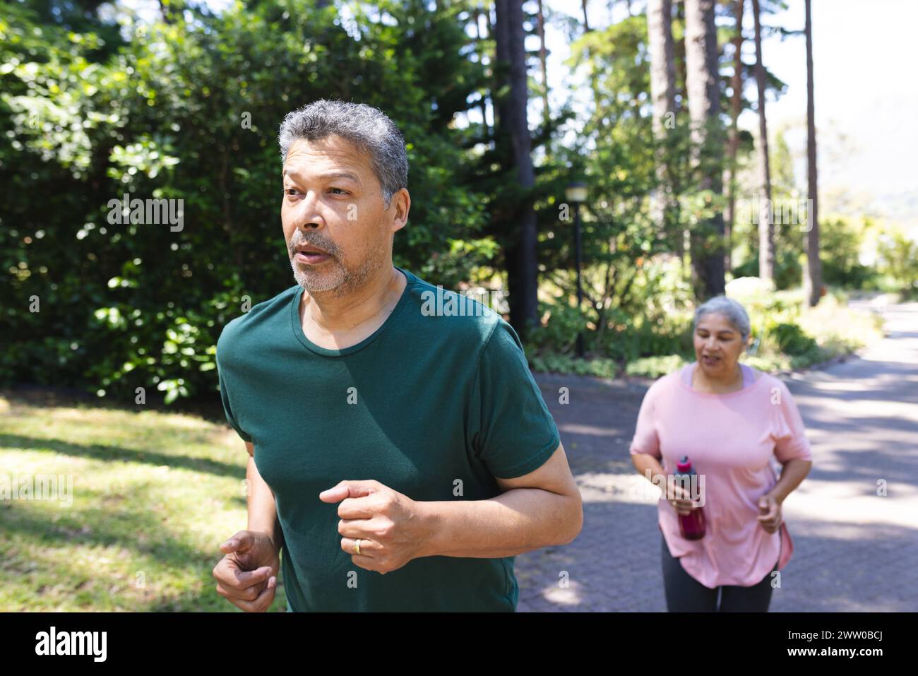 Unalt A senior biracial couple is jogging together outdoors. The man leads ...