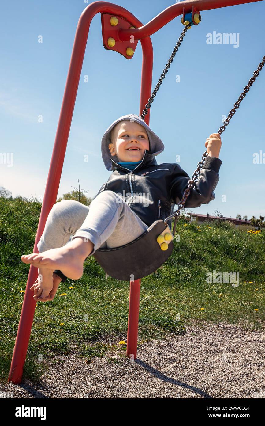 Little cute smiling boy swings on the swing. Stock Photo