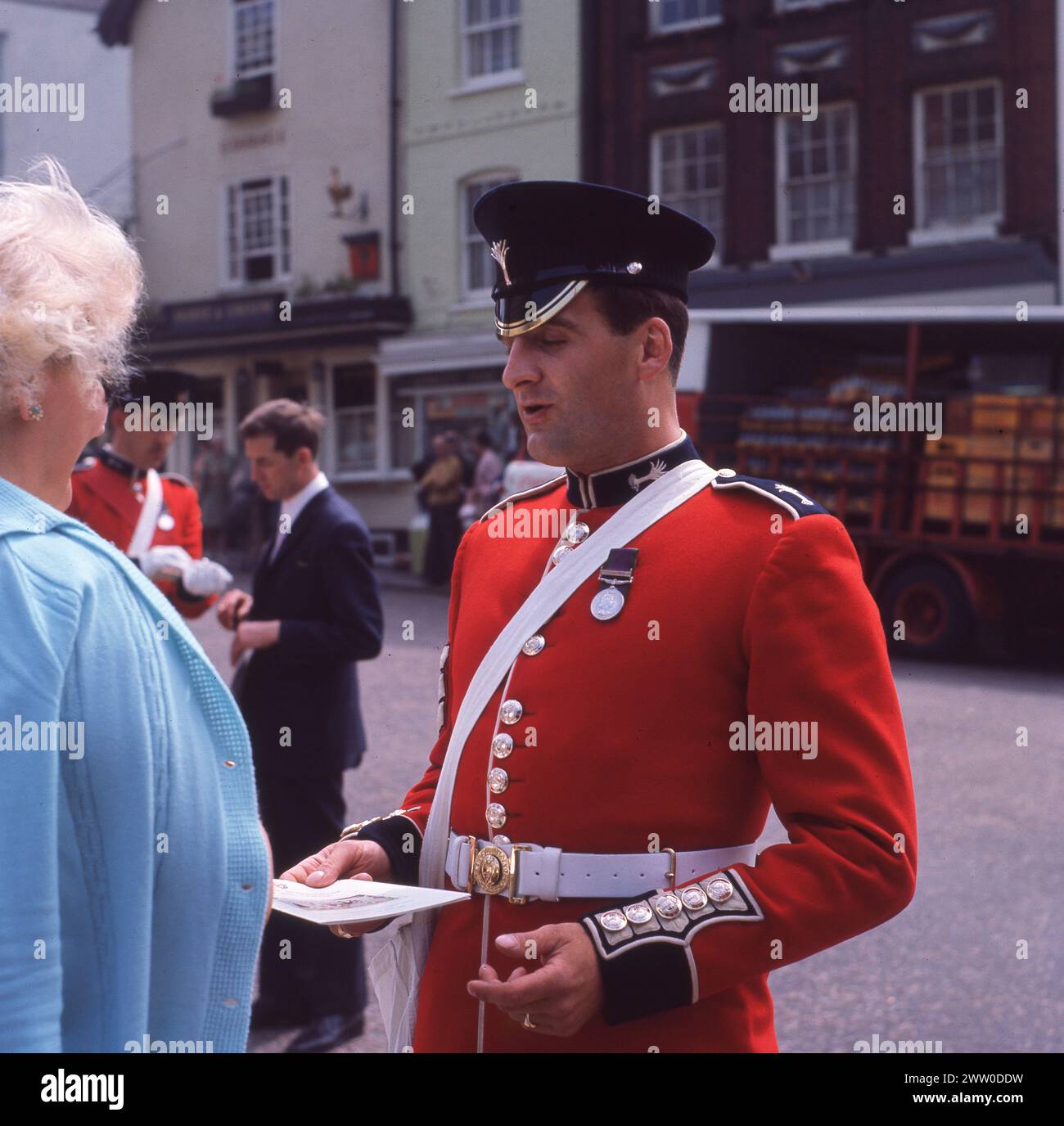 1960s, historical, a uniformed Irish Guard in tunic and forage cap in attendance for 'The Most Noble Order of the Garter,' a special ceremonial event taking place at WIndsor Castle, Berkshire, England, UK, giving an order of service leaflet to a lady guest. Formed in 1900 by Queen Victoria, the Irish Guards is a regiment of the British Arrmy and part of their duties is to guard the British Royal Family and to take part in the traditional ceremonial occasions. Stock Photo