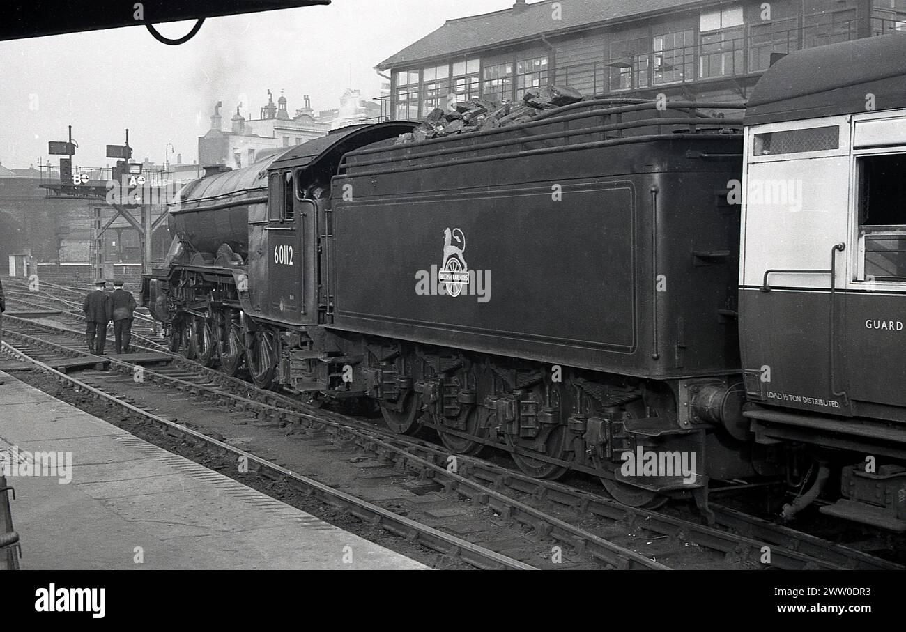 1950s, historical, Briitsh Railways steam locomotive, 60112 on the rail track , coal wagon full, sitting in station, England, UK, guard and driver walking across track. Built for the GNR, the A3 Class Gresley designed locomotive was introduced in 1923, transfering to LNER the following year and later onto the new British Railways in 1948. Stock Photo