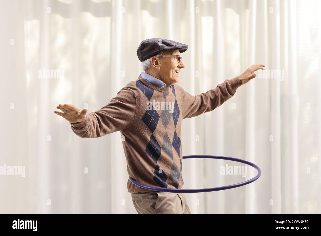 Cheerful elderly man having fun and spinning a hula hoop at home Stock Photo