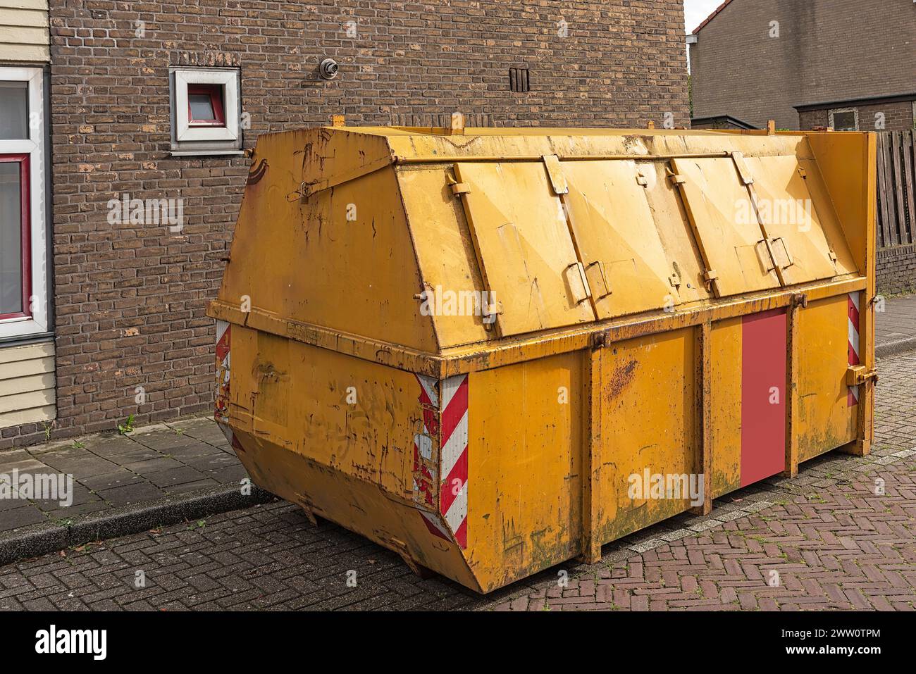 yellow steel industrial waste container with closed shutters stands outside in a parking lot in a residential area Stock Photo