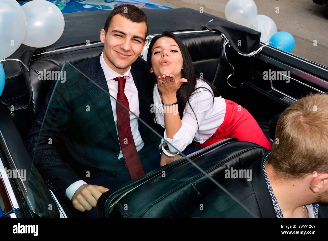 Happy carefree couple graduates posing in a convertible car decorated with baloons before going to their prom party in Sofia Bulgaria, Europe, EU Stock Photo