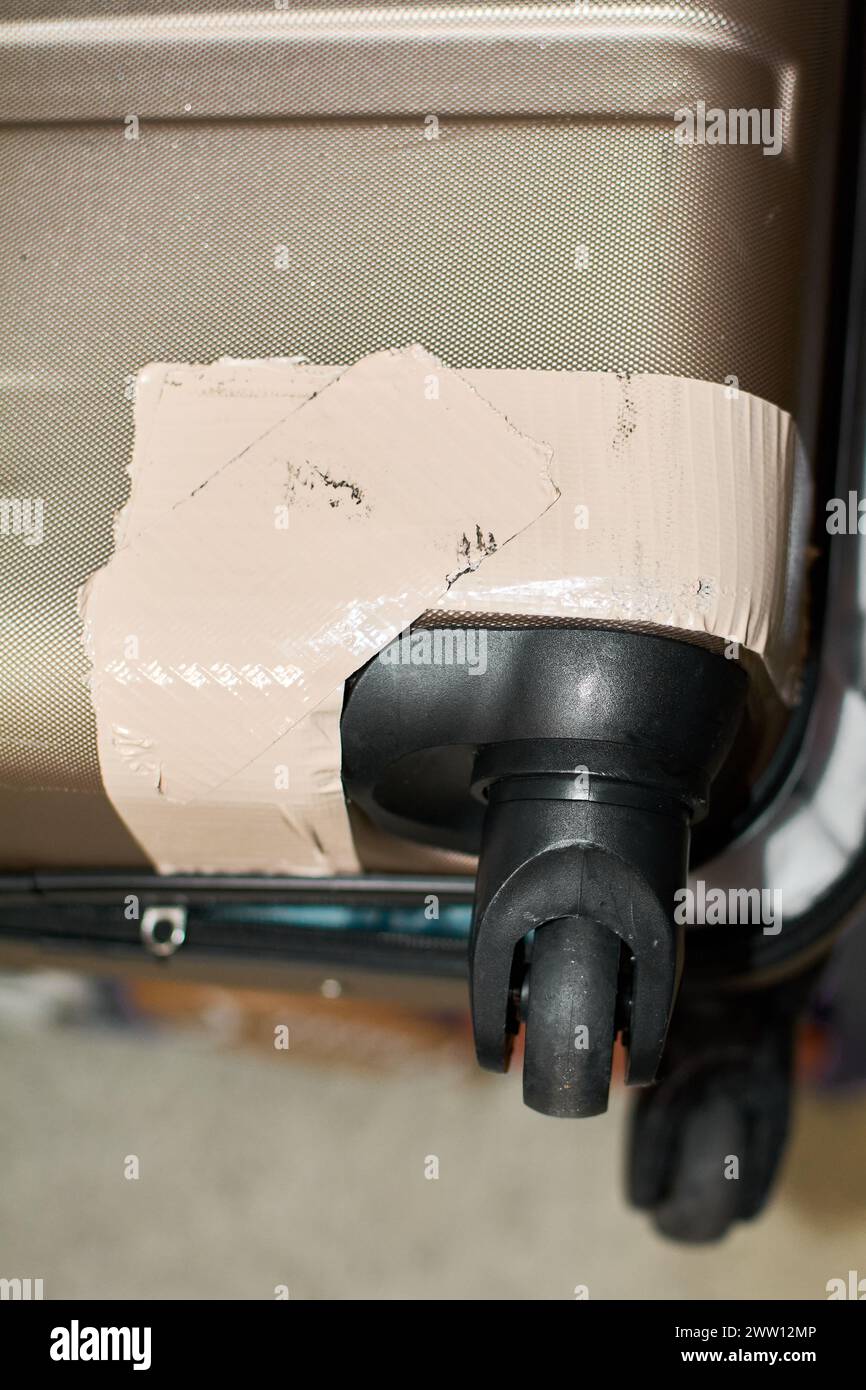 Suitcase wheel and corner secured with tape, indicating damage and quick repair. Stock Photo