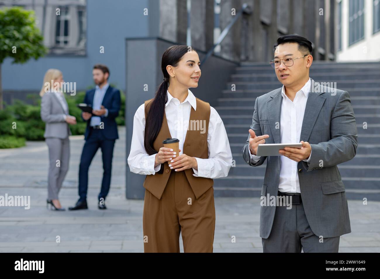 A group of corporate associates in a casual meeting outside. They converse over coffee with a digital tablet in hand. Stock Photo
