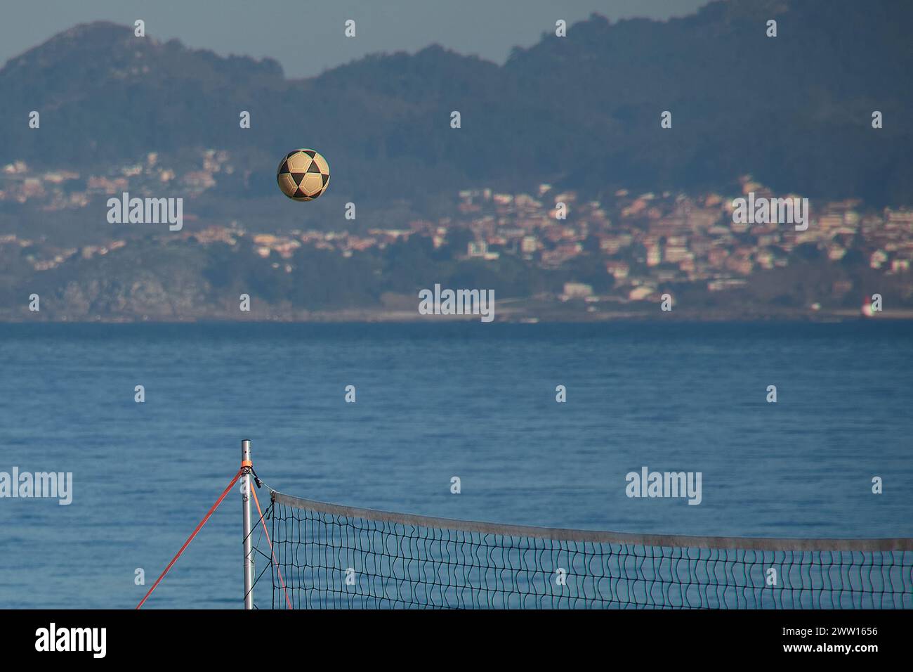 A beach volleyball rises under the net on the Vao de Vigo beach with the Estuary and the Morrazo peninsula in the background Stock Photo