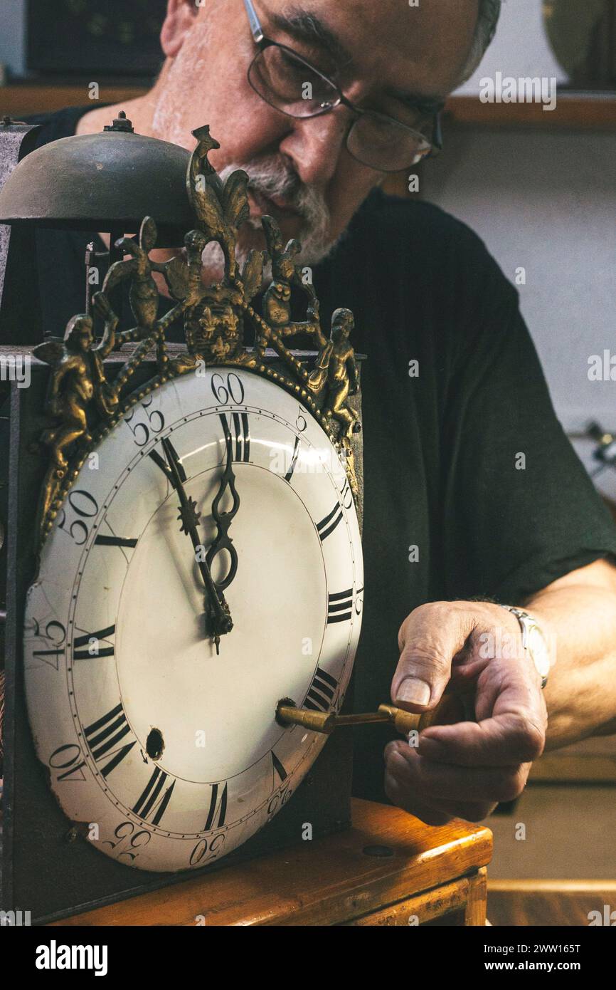 Clockmaker winding up a large wall clock in his watchmaker's shop Stock ...