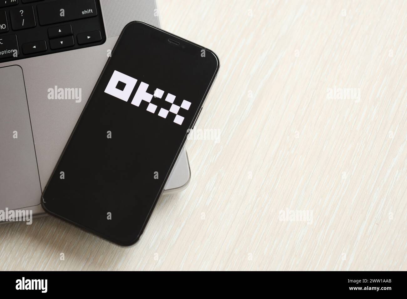 KYIV, UKRAINE - MARCH 15, 2024 OKX logo on iPhone display screen on MacBook panel. Cryptocurrency exchange portal logo on iPhone display screen with dollars and bitcoins on MacBook. Cryptocurrency exchange portal Stock Photo