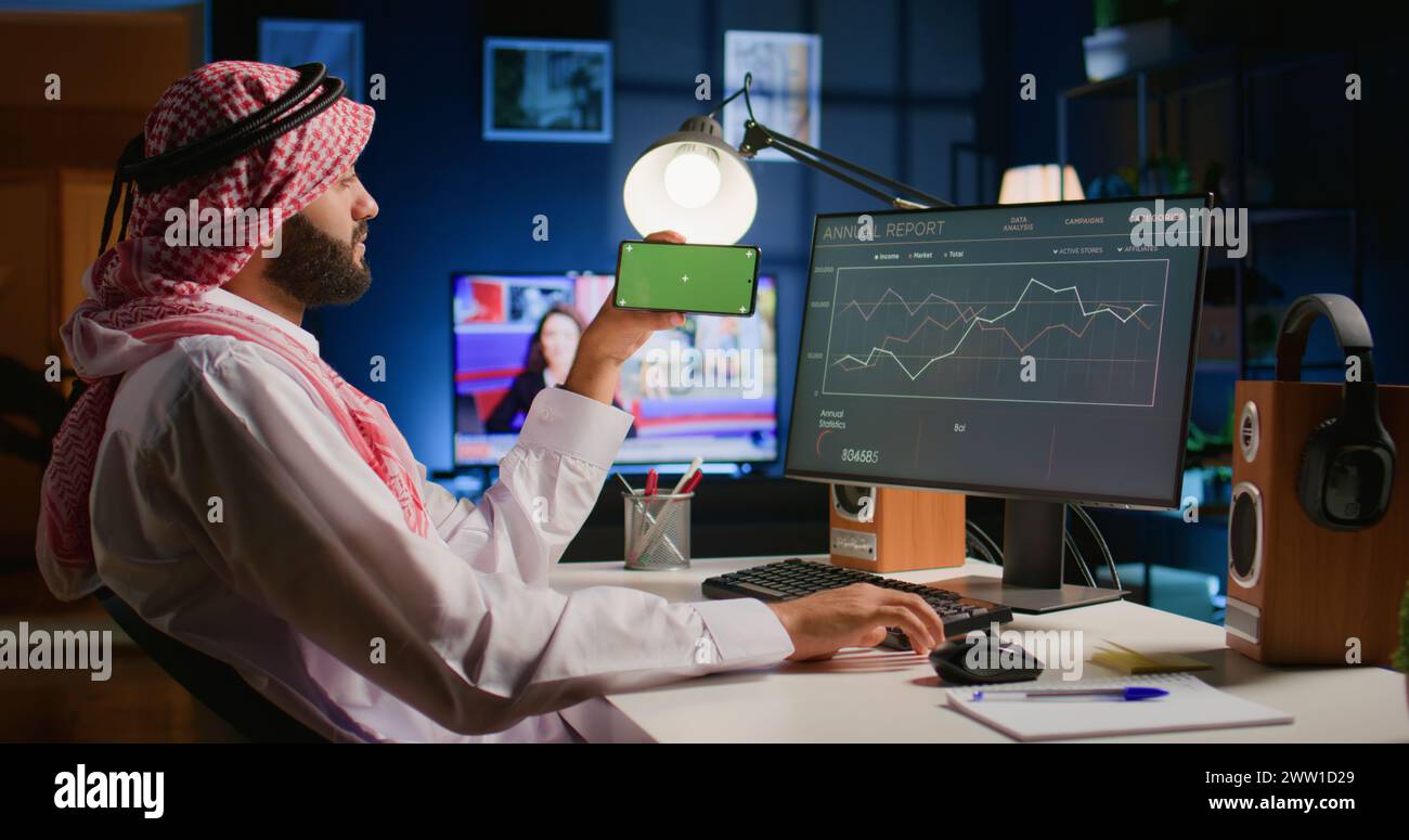 Arab man watching video on green screen cellphone while looking at ...
