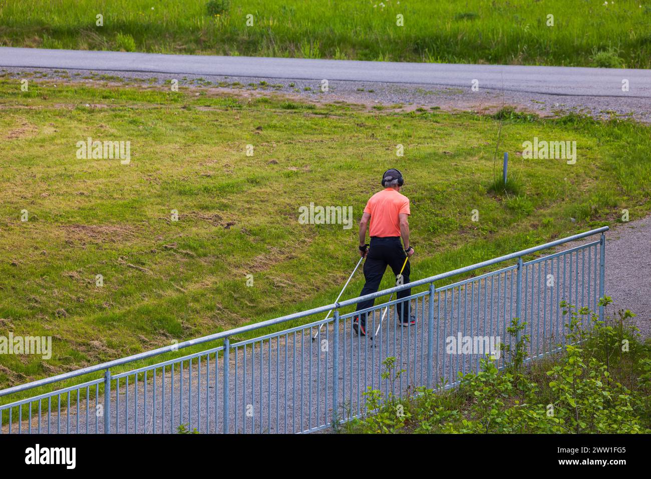 A man on a promenade with Nordic walking poles, navigating a suburban landscape on a summer day. Sweden. Stock Photo